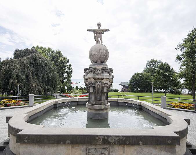 Brunnen mit Zeppelinmännchen in der Mitte und im Hntergrund Bäume.